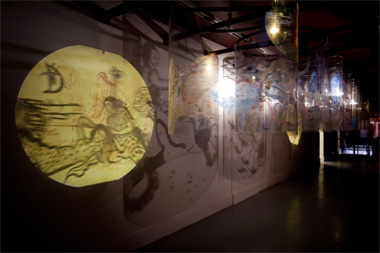 Nalini Malani,   Remembering Mad Meg,   2007 ,  1500 by 500 cm (adaptable),  Two channel shadow/video Play. 2 DVD’s not in sync, Eight rotating Lexan cylinders with metal framework and motors, Installation view Irish Museum of Modern Art, Dublin, Photo © Denis Mortell; courtesy IMMA